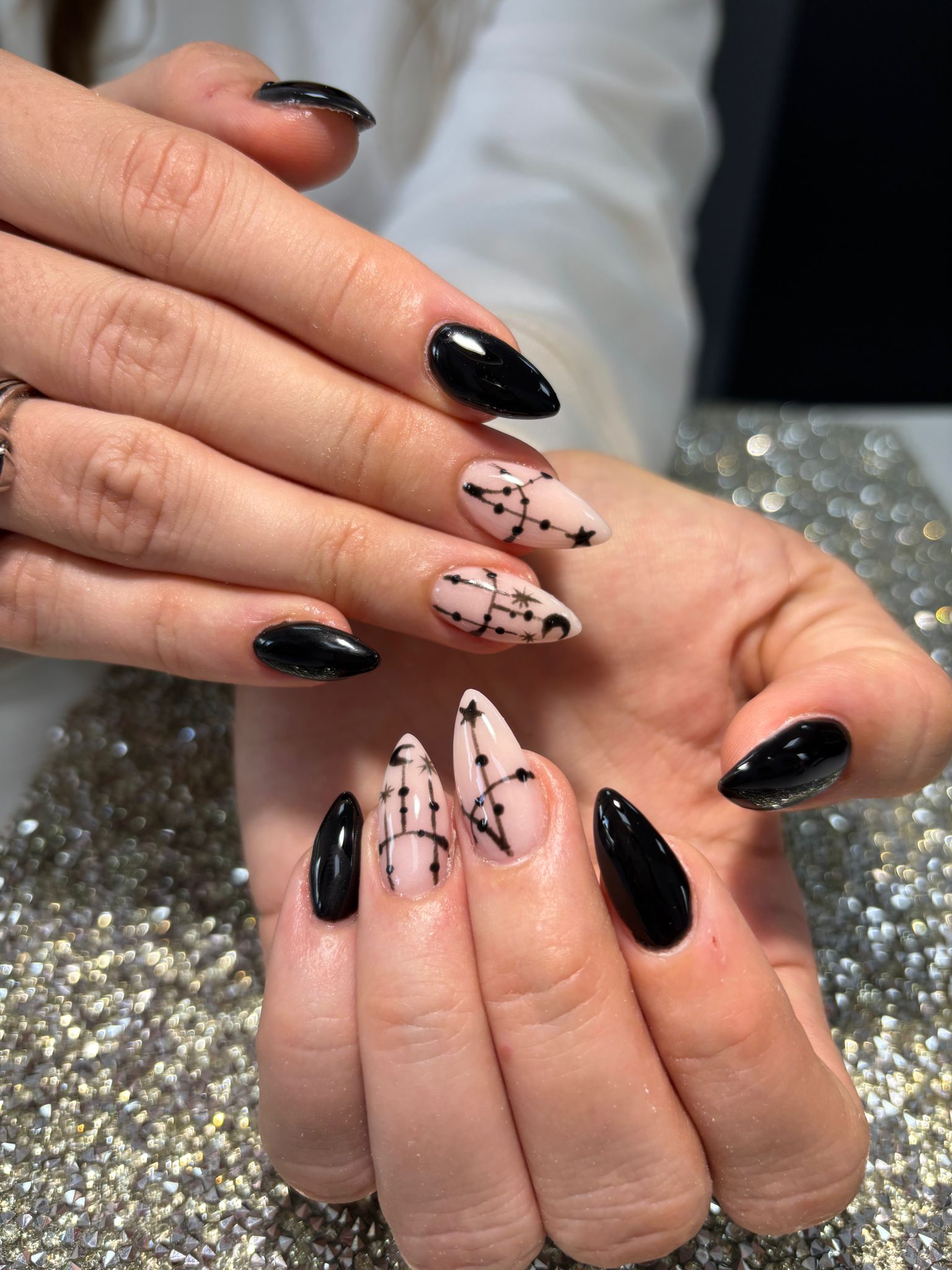 Zwarte en nude amandelnagels met sterrenbeelden op glitter
