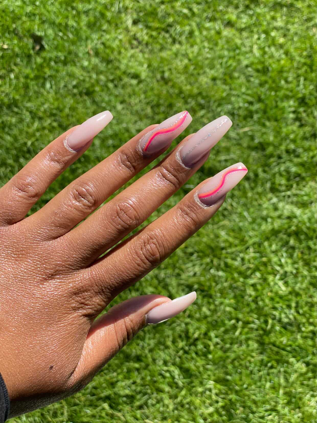 Nude nagels met roze golfjes, hand op het gras