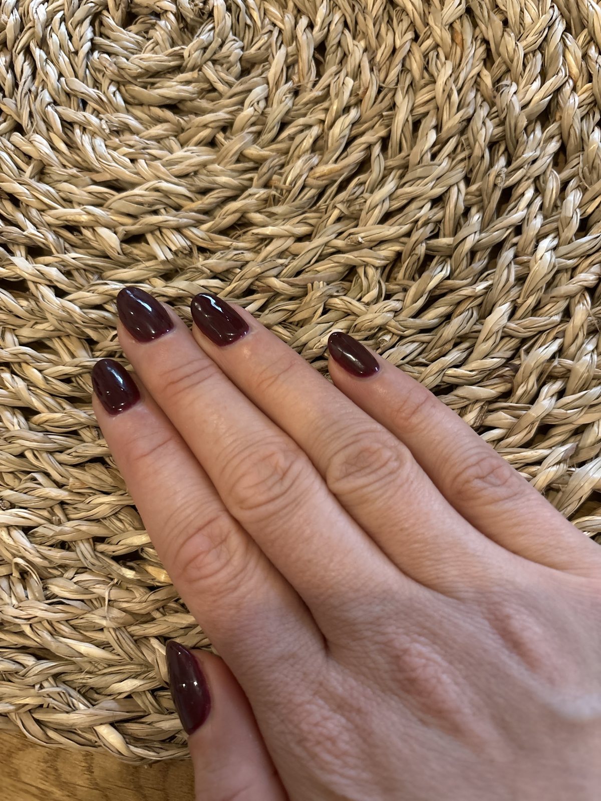 Donker bordeauxrode nagels op een gevlochten mat